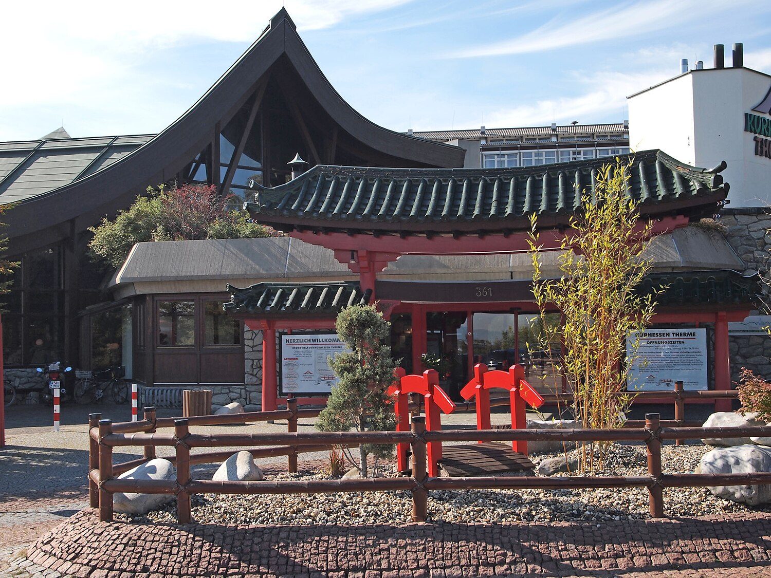 Eingang der Kurhessen Therme in Kassel: Pavillon mit geschwungenem grünem Dach im asiatischen Stil, davor ein Steingarten mit roten Figuren