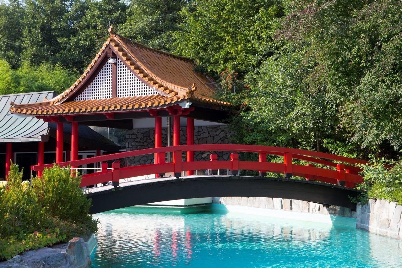 Außenbecken der Taunus Therme in Bad Homburg: rote Bogenbrücke über türkisfarbenem Wasser vor einem Pavillon mit geschwungenem Ziegeldach