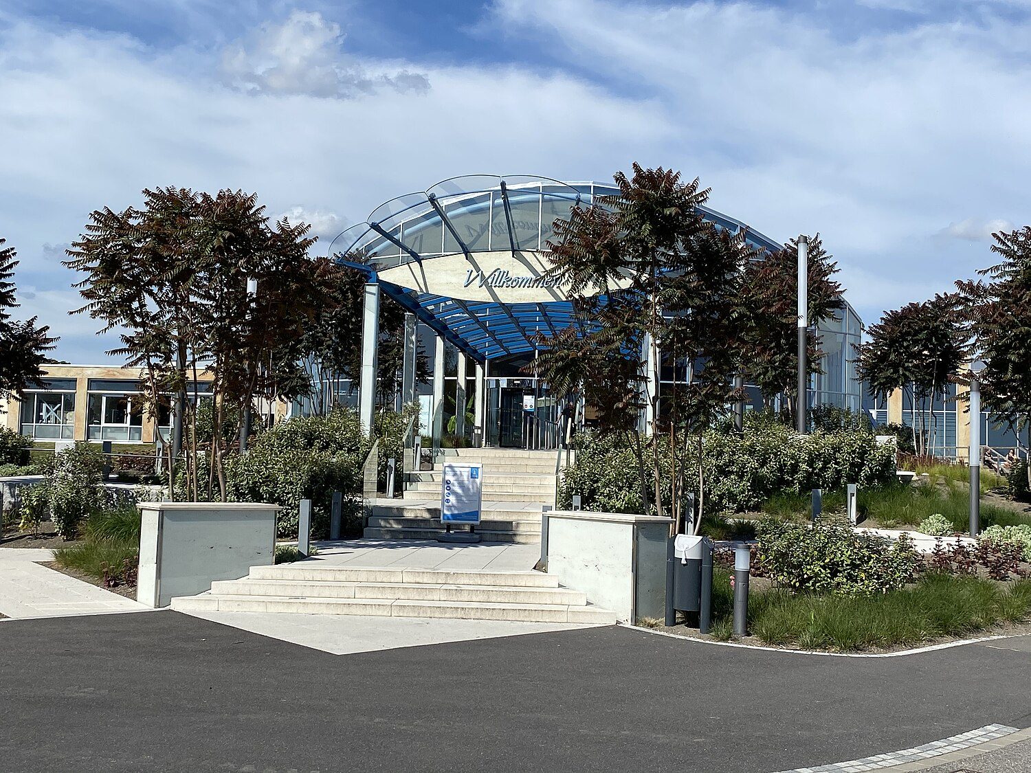 Eingangsportal der Therme Euskirchen: gläserne Kuppel hinter Palmen, davor Stufen und bepflanzte Beete