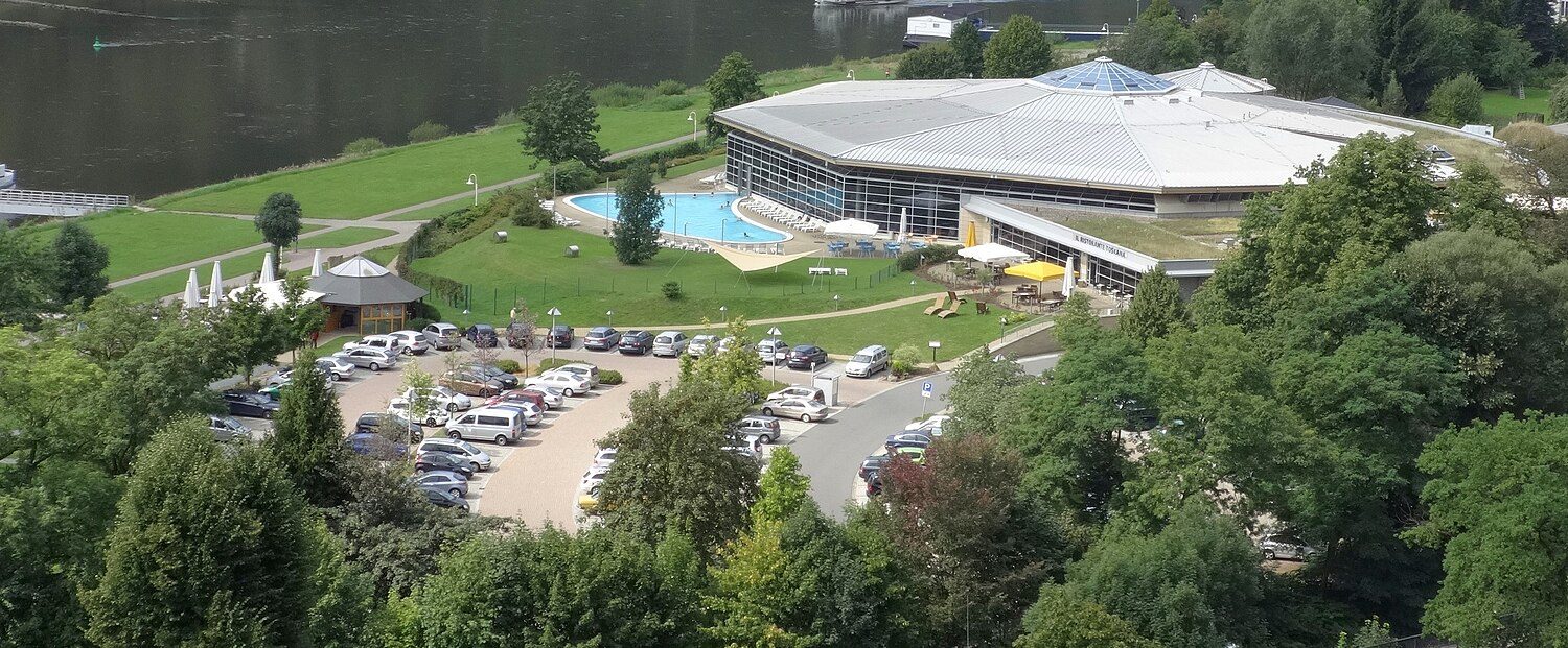 Die Toskana Therme Bad Schandau von oben: flacher Rundbau mit Außenbecken und Liegewiese, umgeben von Bäumen
